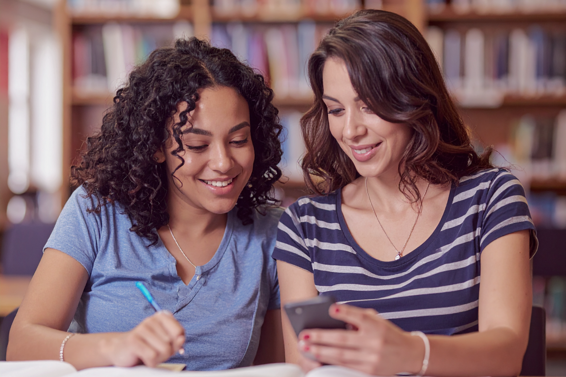 Two language learners studying together and comparing pronunciation waveforms on phone in library